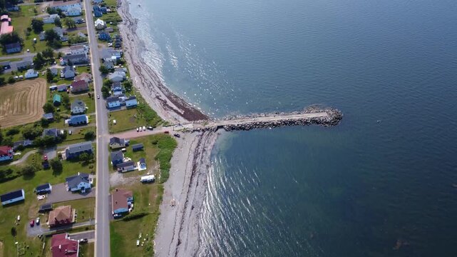 Aerial view of an old abandoned wharf jutting into the calm waters of the St. Lawrence River from the sandy beach of the coastal village of Baie-des-Sables, Quebec, Canada, 2025.