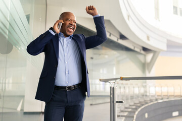 Excited mature African American businessman celebrating success while talking on cellphone....