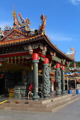 Obraz premium Colorful Chinese Temple Exterior with Dragon Carvings, Ornate Roof Decorations, Red Columns and Traditional Asian Architecture Under Bright Blue Sky at Cultural Heritage Site in Malaysia
