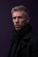 Fototapeta premium Mature caucasian male with gray hair and beard in black coat against purple background