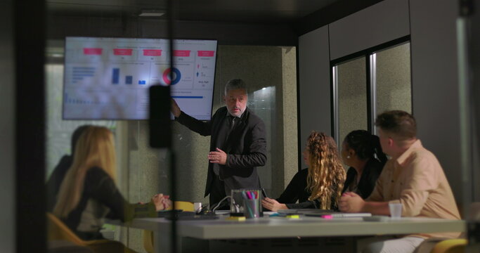 Business executive presenting analytics to diverse team in glass-walled office conference room during strategy meeting - Powered by Adobe