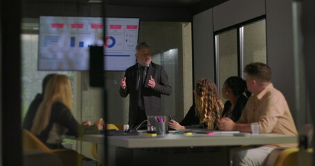 Business executive presenting analytics to diverse team in glass-walled office conference room during strategy meeting