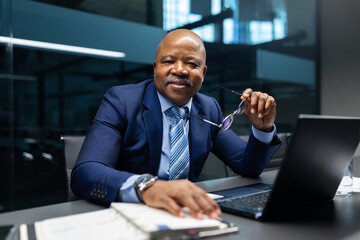 A mature African American businessman holding his glasses and looking confidently at the camera in a modern office, symbolizing leadership, trust, and professional success
