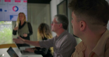 Businesswoman gesturing while speaking during presentation with team watching in corporate conference room featuring data dashboard