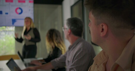 Businesswoman gesturing while speaking during presentation with team watching in corporate conference room featuring data dashboard