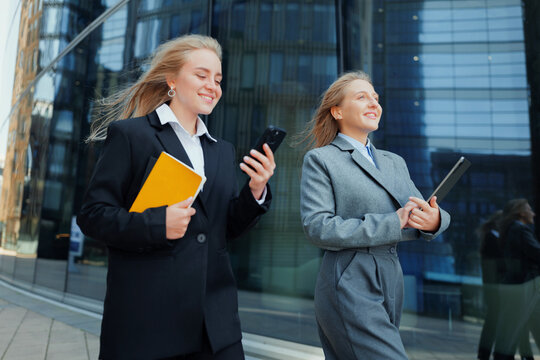 Two women walk confidently outside a modern building