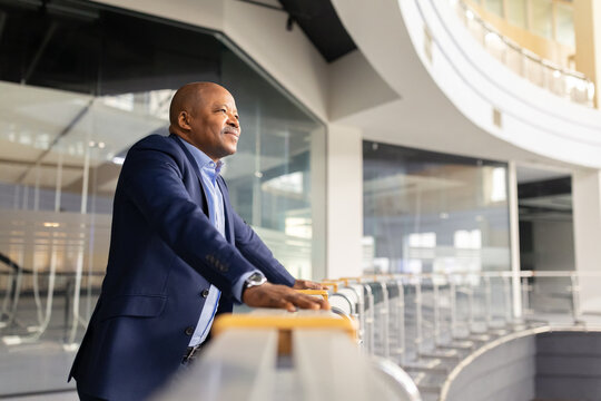 Mature African American businessman standing indoors and looking ahead with a thoughtful smile. Confident executive reflecting on goals and future opportunities in a modern building - Powered by Adobe