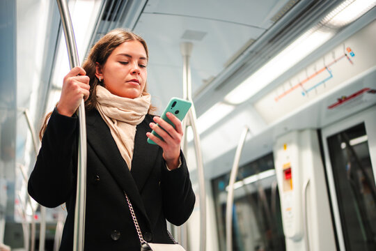 A focused woman using her smartphone while traveling on the subway, highlighting her engagement with technology during her commute, showcasing the integration of mobile applications in everyday travel