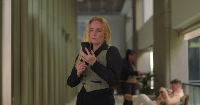 Businesswoman holding phone to ear while talking on a call in office hallway, smiling and walking during informal conversation - Powered by Adobe