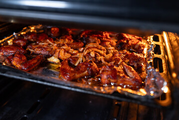 Chicken wings in sauce with onions baking in a heated oven. Foil with appetizing wings and onions in the oven, the baking process, home cooking, and the creation of a delicious meat dish