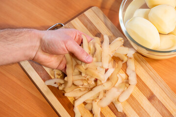 Man's hand cleaning potato peelings. Close-up of a hand collecting peelings from the board near a...