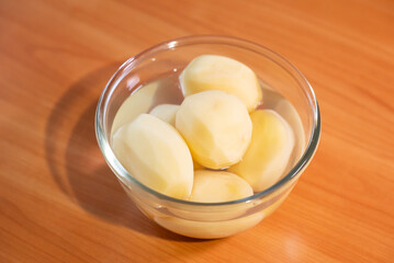 Freshly peeled potatoes resting in a glass bowl filled with clean water. Close-up of ready-to-cook vegetables in water, symbolizing healthy eating and the completed preparation of ingredients