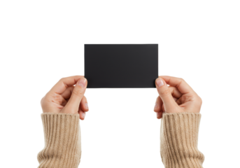 Two light-skinned female hands in a beige knitted sweater gently hold a blank matte black card, isolated on a bright white background with copy space, professional presentation concept