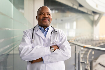 Smiling mature African American doctor standing confidently with arms crossed in a bright modern interior. Professional physician conveying warmth, trust and medical expertise