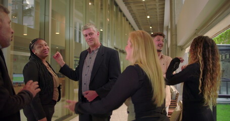 Business team casually talking in modern office hallway, diverse coworkers standing together and engaging in relaxed conversation during informal workplace moment