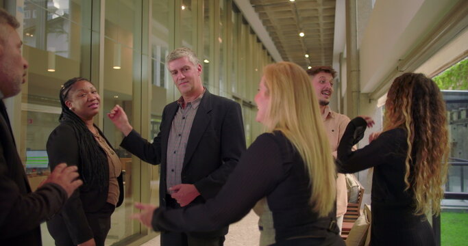Business team casually talking in modern office hallway, diverse coworkers standing together and engaging in relaxed conversation during informal workplace moment