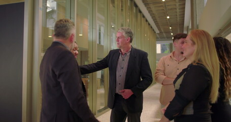Business team casually talking in modern office hallway, diverse coworkers standing together and engaging in relaxed conversation during informal workplace moment