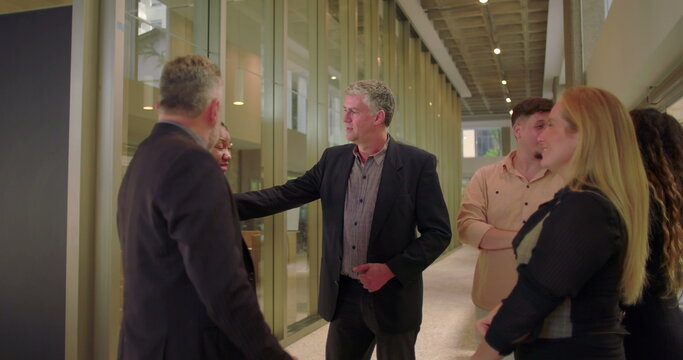 Business team casually talking in modern office hallway, diverse coworkers standing together and engaging in relaxed conversation during informal workplace moment