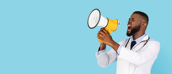 Medical News. Angry black male doctor in uniform screaming with megaphone, emotional african american physician with loudspeaker standing isolated over blue background, panorama, copy space