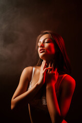 Fototapeta premium Seductive woman posing in lingerie illuminated by red neon light in a dark setting
