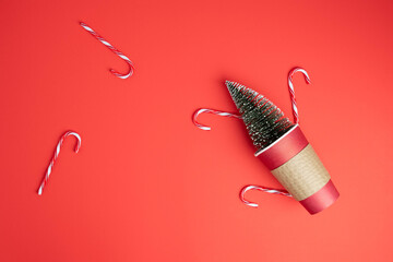 Festive Christmas flat lay with paper coffee takeout cup with a miniature evergreen tree and candy canes on a bright red background. Peppermint mocha.