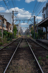 Fototapeta premium Symmetrical tracks run through a quiet Osaka neighborhood, with wooden houses, small platforms, catenary wires, and poles guiding the gaze to a distant vanishing point.