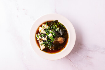 Fresh traditional miso soup with tofu, shiitake mushrooms, green onion, sea mustard and spices on white background with copy space for your design. Traditional Japanese cuisine. 
