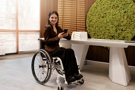 Stylish businesswoman in wheelchair using smartphone at modern office