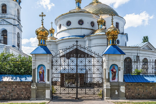 Ornate entrance gate to the Ascension Orthodox Church with icons, golden domes, and decorative wrought iron pillars showcasing traditional architecture. Romny, Ukraine – June 29, 2024