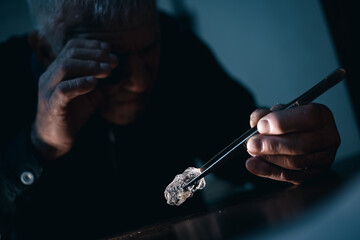 Elderly jewelry caucasian male examining uncut diamond with loupe in low light