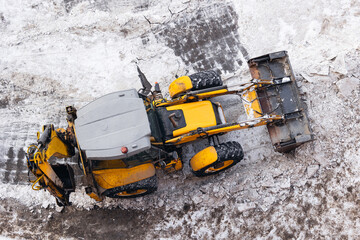 Yellow tractor clearing snow on icy terrain from aerial view