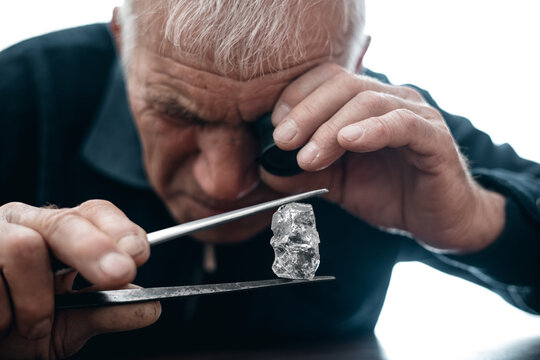 Mature caucasian male jeweler examining large uncut diamond with magnifying loupe