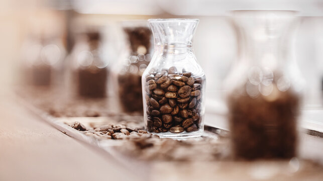 Fresh coffee beans after roasting in glass bottle for variety selection, blurred background