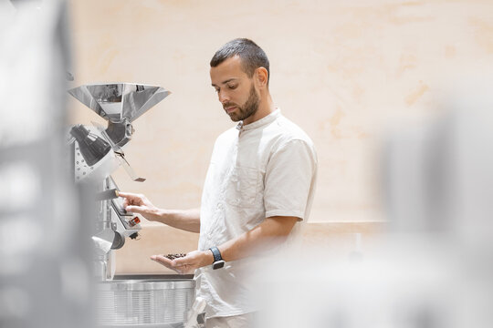Young caucasian male worker operating coffee roasting machine with tablet computer in factory setting.