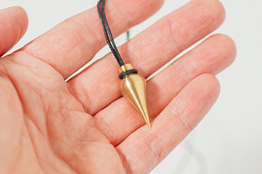 Brass pendulum for dowsing and energy work held in hand. - Powered by Adobe
