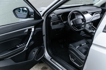 Modern black leather car interior with open driver door, showcasing dashboard