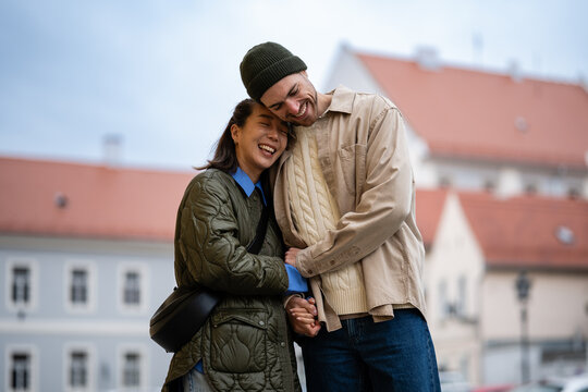 Happy diverse couple embracing laughing in city