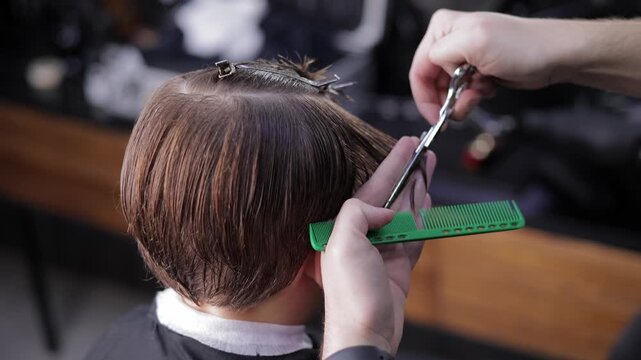 Male child haircut in salon barber shop with stylist using scissors and comb.