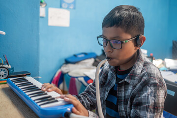 Mexican boy with glasses and hearing aid playing melodica, learning music