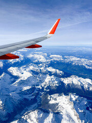 Fototapeta premium Airplane wing above snow-capped mountains, showcasing breathtaking aerial view of rugged terrain, with clear blue sky and distant peaks, creating a sense of adventure and exploration