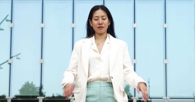 Serious portrait video of a young Asian businesswoman looking directly at the camera with crossed arms in a modern urban setting.