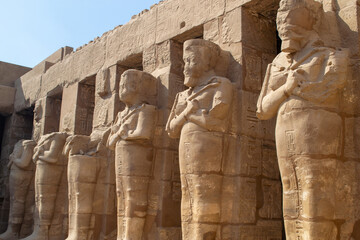 Egypt, Luxor, 01.02.2022.Ancient Egyptian stone statues standing and seated among sandstone temple ruins with carved hieroglyphs and warm light, Karnak temple.