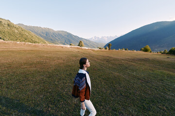 Fototapeta premium Woman walking in a mountain meadow, hiking with a backpack across open landscape and nature scenery, enjoying solitude and fresh air during outdoor exploration.