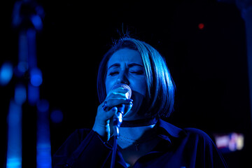 Female caucasian singer performing on stage under dramatic blue lighting