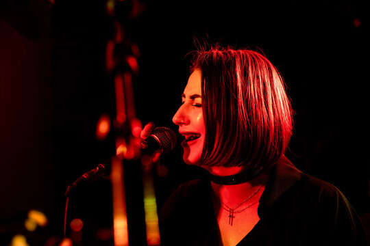 Female caucasian young singer performing live on stage with red lighting - Powered by Adobe