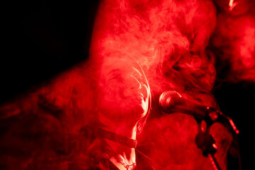 Female singer performing in red smoke with microphone in dramatic lighting