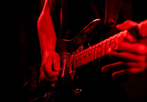 Close-up of guitarist playing electric guitar on stage in red lighting