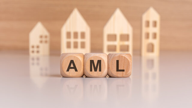 wooden cubes spelling AML in front of model houses, symbolizing anti-money laundering