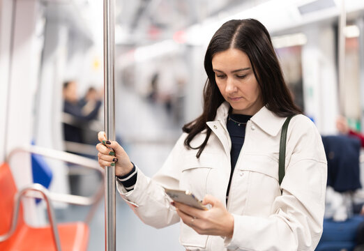 Woman passenger travels in the subway car and uses a mobile phone to communicate on social networks
