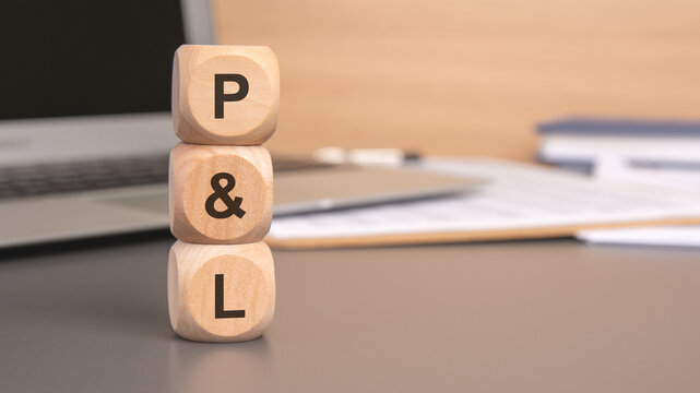 wooden blocks spelling P L on a desk, symbolizing profit and loss in business finance